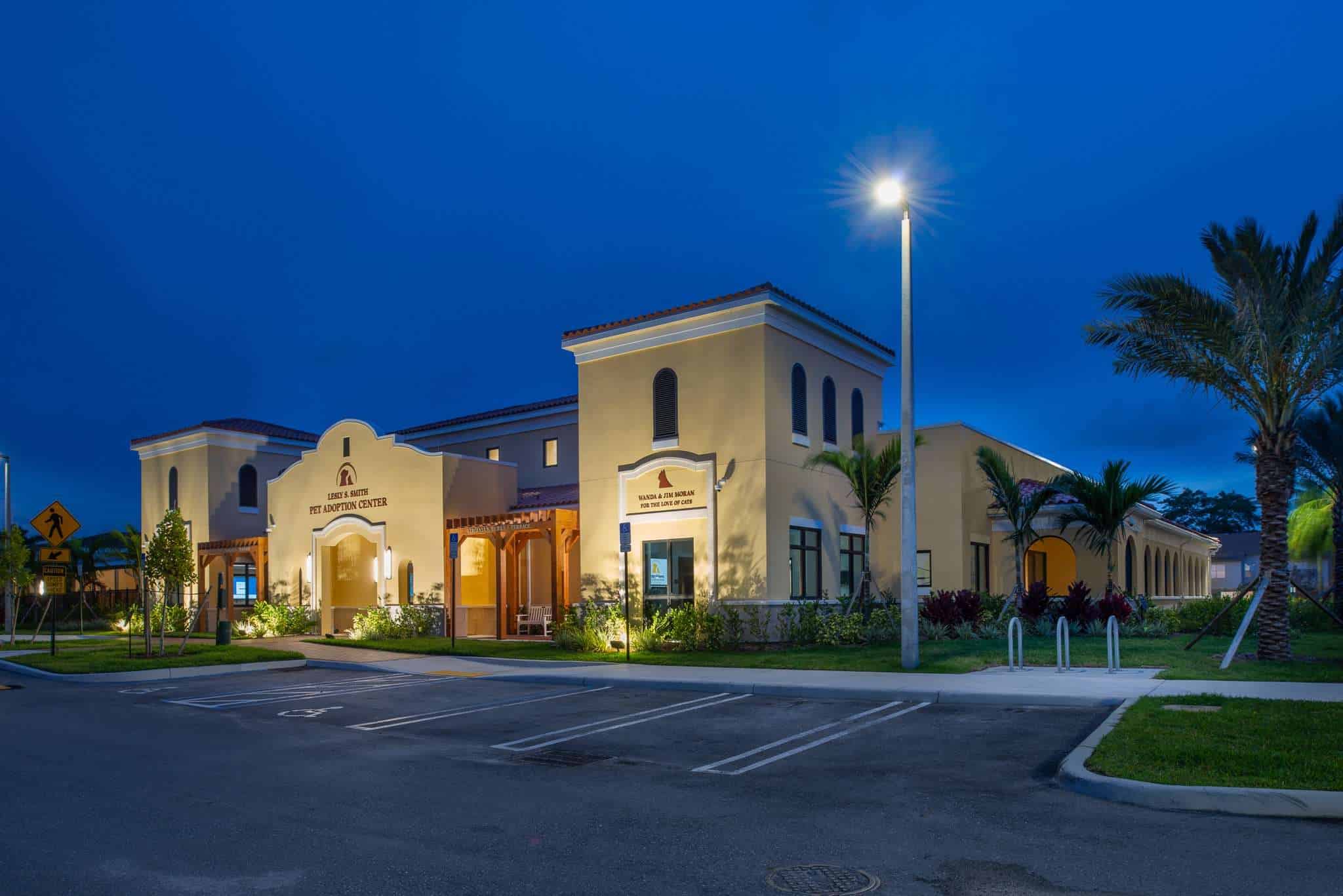 Animal shelter building at dusk with well-lit entrance and palm trees.