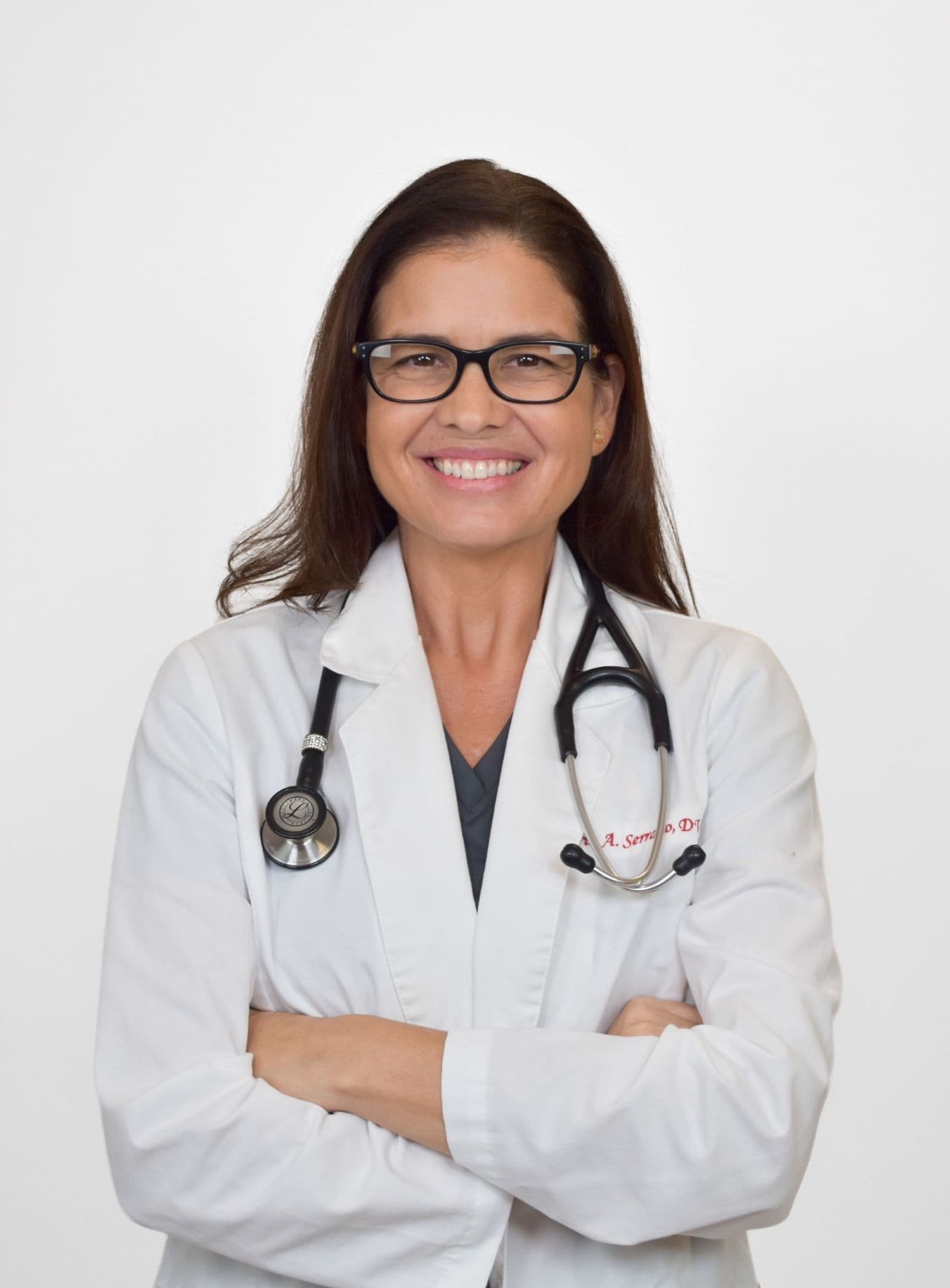 Female veterinarian smiling with arms crossed, wearing glasses and stethoscope.
